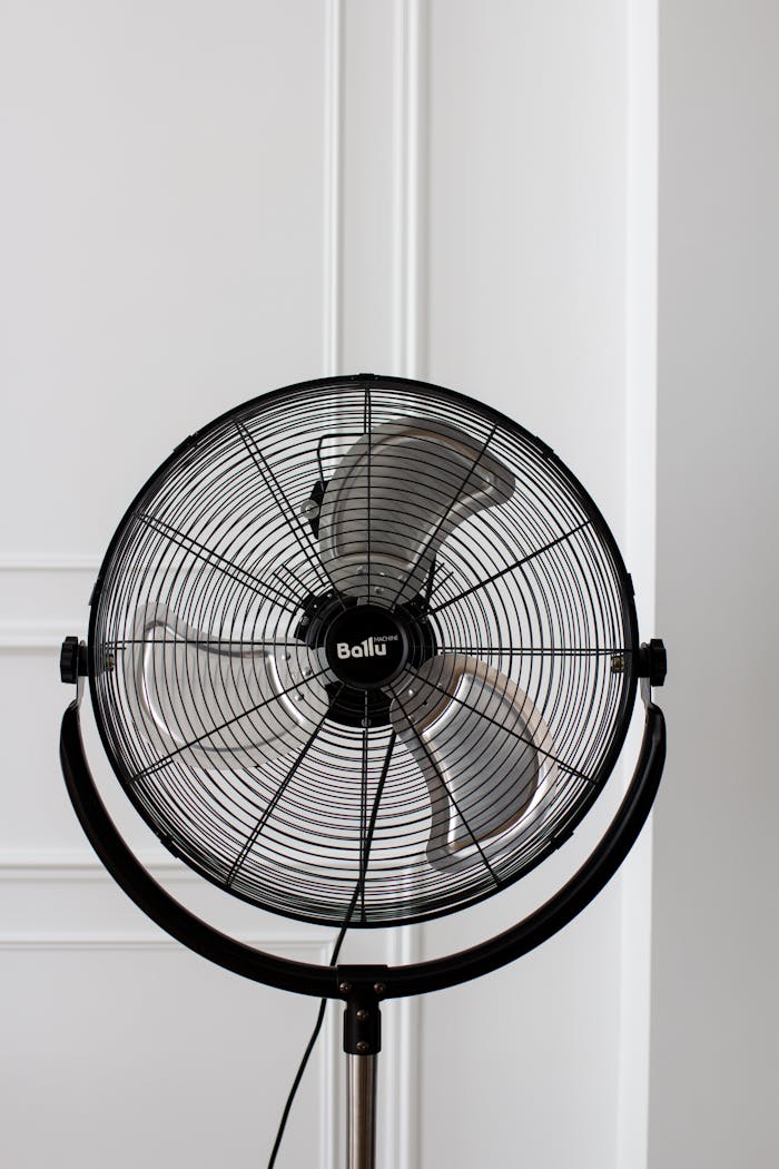 about-01 Black stand fan with industrial design against a white wall, offering modern home cooling solutions.