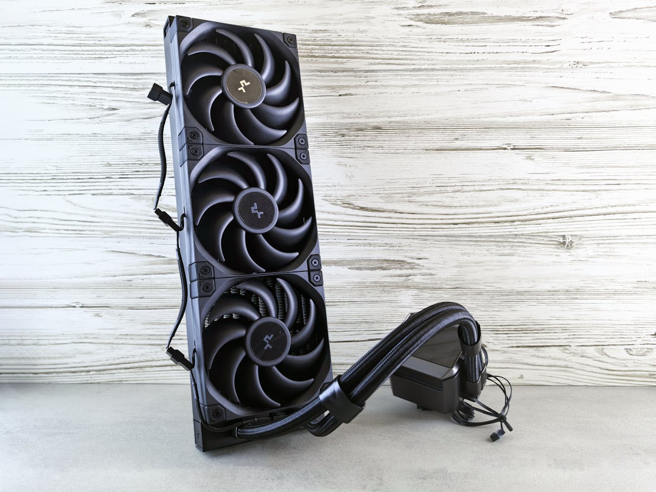 hero-img-01 Triple fan liquid CPU cooler in a modern, minimalist setup against wood grain background.