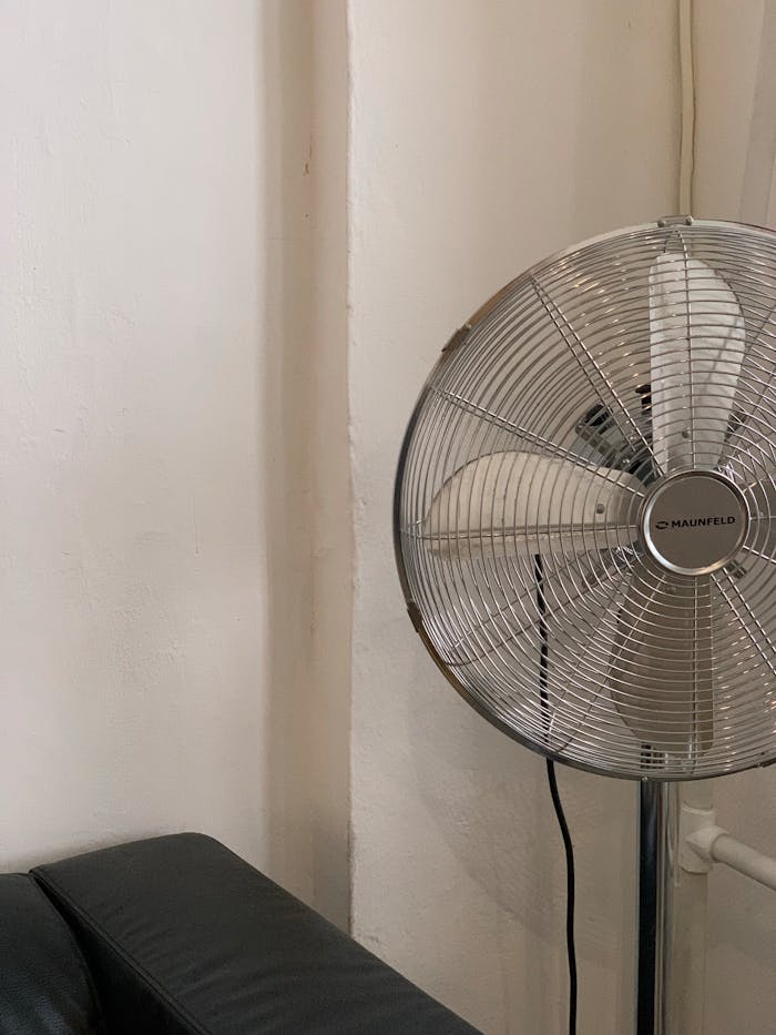 services-02 A modern metal fan stands in a minimalistic interior with a couch.